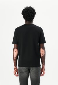 T-shirt noir à manches courtes avec un col rond. Présente une texture lisse, un design simple et une coupe décontractée. Porté avec un jean gris.