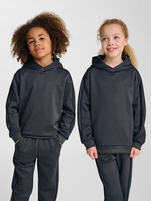 Zwei Kinder stehen nebeneinander und tragen passende dunkelgraue Kapuzen-Sweatshirts und Hosen, mit den Händen in den Taschen oder entspannt an den Seiten.
