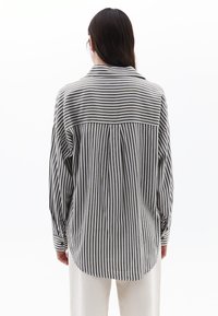 Camicia a righe grigia e bianca, con maniche lunghe, colletto e una vestibilità rilassata. Il tessuto appare leggero e con una texture.