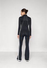 Zwarte sportoutfit met een nauwsluitend long-sleeve shirt met hoge kraag en gestreepte accenten, gecombineerd met uitlopende broek.