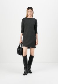 Γκρι εφαρμοστό φόρεμα με τρία τέταρτα μανίκια, συνδυασμένο με μαύρες δερμάτινες μπότες μέχρι το γόνατο και μια υφασμάτινη μαύρη τσάντα. Μινιμαλιστικός σχεδιασμός.