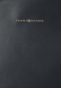 Svart teksturert lær lommebok med et gullpræget "TOMMY HILFIGER"-logo på forsiden. Kompakt design, elegant overflate og subtile detaljer.