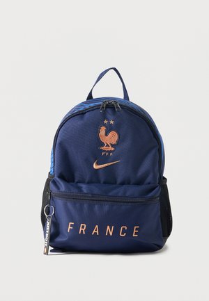 Sac à dos bleu marine avec emblème de la France, coq doré et logo Nike, poche avant zippée avec texte « FRANCE » et poches latérales en filet.