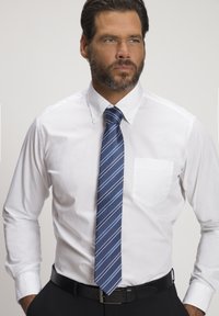 Weißes Hemd mit Knopfleiste und einer linken Brusttasche, kombiniert mit einer blauen gestreiften Krawatte. Der Gürtel ist schwarz, und der Hintergrund ist schlicht weiß.
