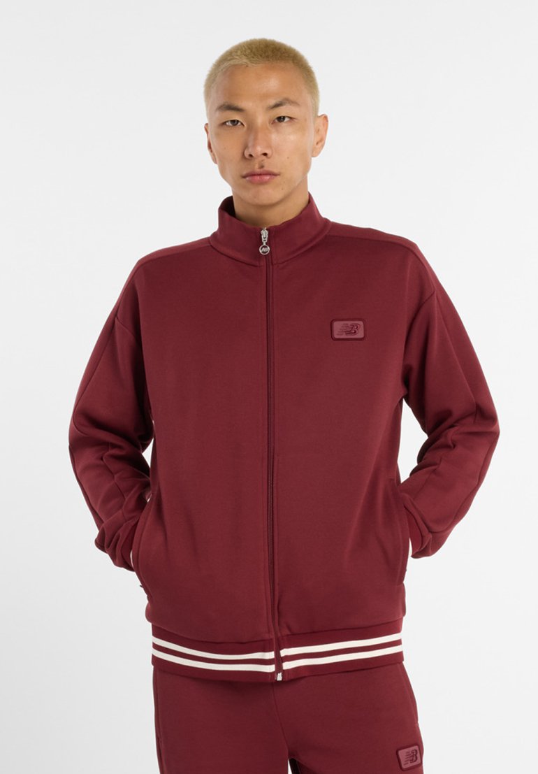 Bordeaux kleurige zip-up jas van zachte stof, met een staande kraag, witte gestreepte accenten aan de onderkant en een klein logopatch op de borst.