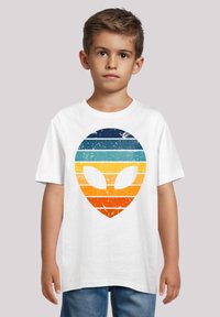 White cotton t-shirt featuring a textured alien head graphic with horizontal stripes in dark blue, light blue, orange, and yellow hues.