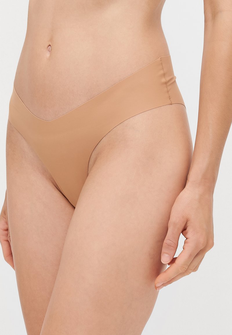 Beige nahtloser Bikini-Unterteil mit einem V-förmigen Bund. Hergestellt aus glattem, dehnbarem Stoff, bietet er minimalen Komfort und saubere Kanten.