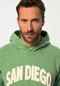 Felpa verde con una texture morbida, caratterizzata da una grande grafica bianca "SAN DIEGO" sulla parte frontale e un cappuccio con cordini.