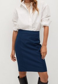 Jupe crayon bleu marine au design ajusté, texture lisse et taille haute. Associée à une chemise blanche à boutons.