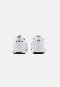 Sneakers din piele albă cu un finisaj neted, având un logo contrastant negru pe lateral și un interior căptușit de culoare bleu deschis. Talpă din cauciuc negru.