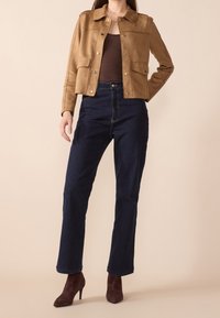 Veste cropped en daim marron avec des boutons-pression, deux poches avant, associée à un jean en denim noir taille haute et des bottes à talons en daim bordeaux.
