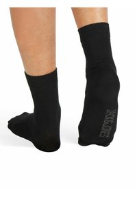 Schwarze Knöchelsocken aus einem weichen, dehnbaren Material. Mit einem gerippten Bündchen und einem Logo-Detail auf der Unterseite. Glatte Textur, keine Muster.