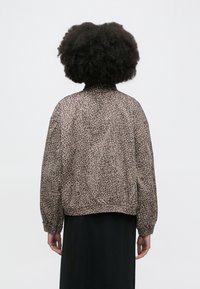 Καφέ bomber μπουφάν με μπεζ ζωικό σχέδιο, ελαστικές μανσέτες και τελείωμα. Η πίσω πλευρά είναι λεία, με στρογγυλή λαιμόκοψη και άνετη εφαρμογή.