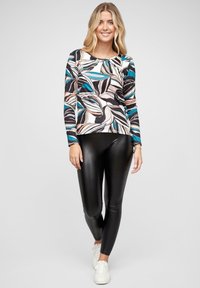 Hosszú ujjú felső színes levélmintával, amely teal, rózsaszín és fekete árnyalatokat tartalmaz. Fekete fényes leggings-szel és fehér sportcipővel párosítva.