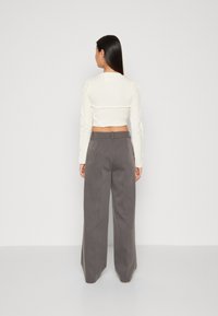 Top corto bianco a maniche lunghe con texture a coste e dettaglio a torsione sul retro, abbinato a pantaloni grigi a gamba larga a vita alta.