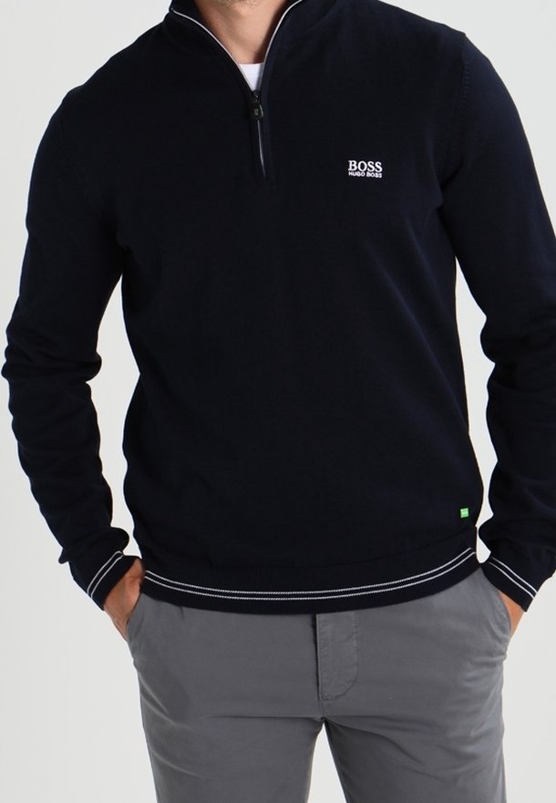 Marinblå tröja med dragkedja vid kragen, ribbade ärmslut och nederkant. Har en liten vit logotyp på bröstet. Tillverkad av ett mjukt, texturerat tyg.