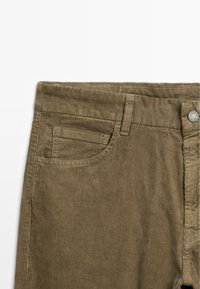 Bruine corduroy broek met een gestructureerd oppervlak, één voorzak en een knoopsluiting bij de taille.
