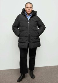 Czarna pikowana kurtka puchowa z kapturem, zapinana na zamek z przodu, z przeszyciami i długimi rękawami. Do tego czarne spodnie za kostkę i sznurowane botki.