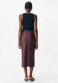 Débardeur noir à côtes avec une jupe midi bordeaux. La jupe est dotée de deux poches arrière et d'une fermeture éclair. Le modèle porte des sandales noires à enfiler.