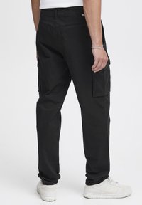 Schwarze Cargo-Hosen mit lockerer Passform, ausgestattet mit Seitentaschen und einem strukturierten Stoff, kombiniert mit weißen Turnschuhen.