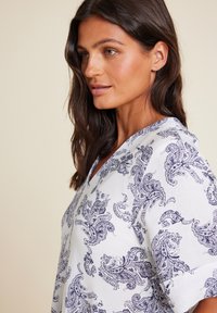 Hvit bluse med et marineblått paisleymønster, V-hals design og rullede korte ermer. Laget av lett stoff.