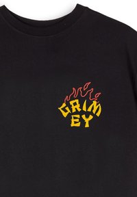 Camiseta de algodón negra con un colorido logo "GRIMEY" en amarillo, contorneado en rojo, con acentos de llamas sobre el texto. Diseño de cuello redondo estándar.