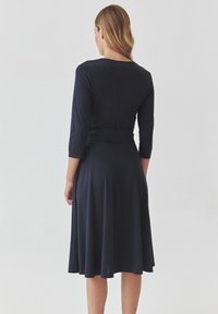 Merenneitomainen sininen mekko pitkillä hihoilla, istuvalla vartalokappaleella ja levenevällä hameella, valmistettu sileästä ja pehmeästä kankaasta. Ominaisuuksiin kuuluu yksinkertainen pyöreä pääntie.
