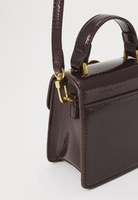 Bordeaux lackläderhandväska med strukturerad design, guldaccenter och ett kort handtag. Slät yta, kompakt storlek.