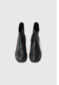 Botas de tobillo de cuero negro con una textura suave, puntera redonda, paneles laterales elásticos y una suela baja de goma. Vista desde arriba.