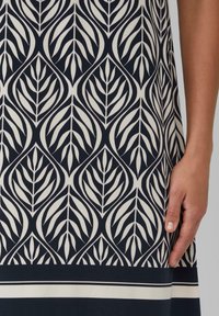Musterkleid mit marineblauen und cremefarbenen Blattmotiven. Glatte Stoffqualität mit taillierter Passform und kontrastierendem horizontalem Streifen am Saum.