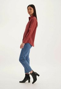 Chemise à carreaux rouges à manches longues, associée à un jean bleu clair et des bottines noires à talons. Design minimaliste, coupe ajustée.