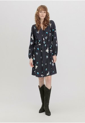 Dunkelblumenkleid mit langen Ärmeln, elastischem Bund und knielangem Saum, das farbenfrohe Blumenmuster auf navyfarbenem Hintergrund zeigt. Kombiniert mit hohen, dunklen Stiefeln.