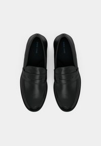 Crne kožne mokasine s glatkom završnom obradom, zaobljenim vrhom i prošivenim detaljima na vrhu. Imaju dizajn bez vezica s neprimjetnim kopčama.