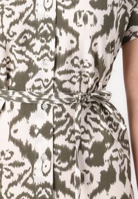 Robe à motifs verts et blancs avec un devant à boutonnage, des manches courtes et une ceinture assortie nouée à la taille. Tissu texturé.