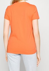 Camiseta corta de mangas en color naranja, hecha de algodón, con un escote redondeado y un diseño ajustado, vista desde atrás.