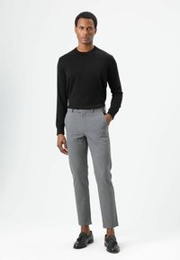 Zwarte trui met ronde hals gecombineerd met lichtgrijze, op maat gemaakte broek en zwarte loafers. De outfit heeft een nauwsluitende pasvorm en een subtiele textuur.