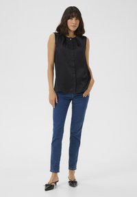 Czarna, bezrękawnikowa satynowa bluzka z okrągłym dekoltem i zapięciem na guziki, zestawiona z niebieskimi skinny jeansami i czarnymi czółenkami w szpic.