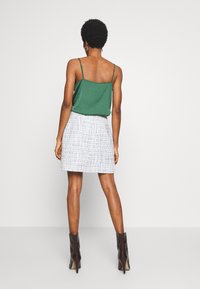 Camisola di raso verde con spalline sottili, abbinata a una gonna bianca strutturata e stivaletti neri con tacco, vista da dietro.