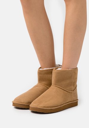 Botas de tobillo de ante color marrón claro con un interior suave y esponjoso, que presentan una puntera redondeada, costuras mínimas y una suela plana de goma.