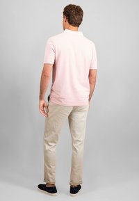 Vaaleanpunainen poolopaita, jossa on klassinen kaulus ja lyhyet hihat, yhdistettynä vaaleanbeigeihin chinohousuihin ja mustiin liukuisiin kenkiin.