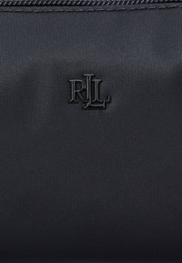 Musta nailonipussi, jossa on teksturoitu pinta ja kiiltävä, kohokuvioitu "RLL"-logo. Suunnittelu on yksinkertainen, ja siinä on vetoketjusuljenta ilman lisäkoristeita.