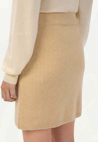 Stickad kjol i ljusbeige med ribbat mönster, har en åtsittande midja och en rak passform som slutar ovanför knäet.