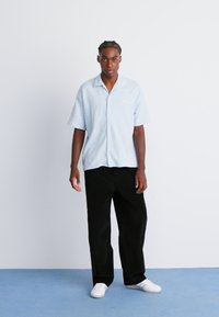 Light blue short-sleeve shirt in textured fabric, paired with loose-fitting black corduroy pants and white sneakers.