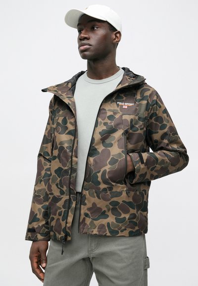 Καμουφλάζ μπουφάν με μείγμα καφέ και πράσινων σχεδίων, με φερμουάρ στο μπροστινό μέρος, κουκούλα και λογότυπο στο στήθος. Ομαλή υφή υφάσματος.