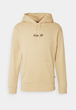 Sudadera con capucha Nike SB beige con bolsillo canguro delantero, capucha con cordón y pequeño logo Nike SB marrón centrado en el pecho.
