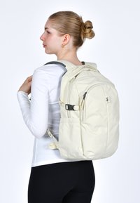 Světle béžový batoh s nastavitelnými popruhy, více zipy a bočními kapsami. Vyrobeno z odolného materiálu s elegantním, moderním designem.