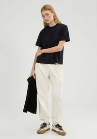 Granatowa bawełniana koszulka o luźnym kroju, z krótkimi rękawami i okrągłym dekoltem, zestawiona z kremowymi dresami i trampkami z brązowymi akcentami.