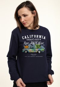 Tmavě modrá mikina s grafikou vintage pickup trucku a graffiti uměním. Text zní "Silnice 1, Kalifornie, Los Angeles."