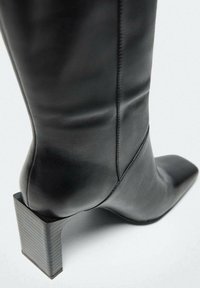 Stivale alla caviglia in pelle nera con tacco quadrato e punta appuntita. Texture liscia con sottili dettagli di cucitura.