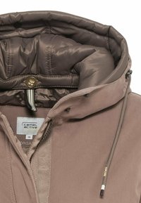 Chaqueta de abrigo marrón con un alto cuello, capucha y cordones ajustables. El material es suave con un forro acolchado y detalles de botones.